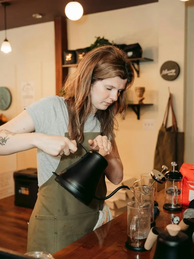 Izzy pouring from a gooseneck kettle into press pots behind the bar